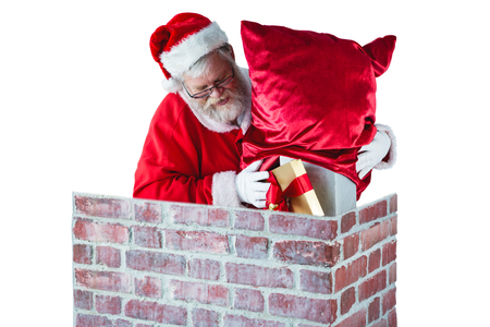 Santa claus placing gift box into a chimney during christmas timeの写真素材