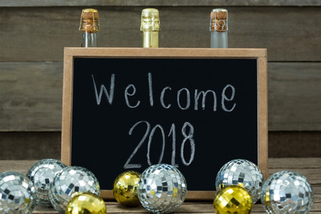 Welcome 2018 written on slate board with baubles and champagne bottle on wooden surfaceの写真素材