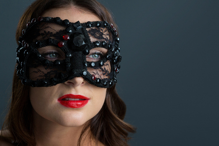 Beautiful woman wearing masquerade mask against black backgroundの写真素材