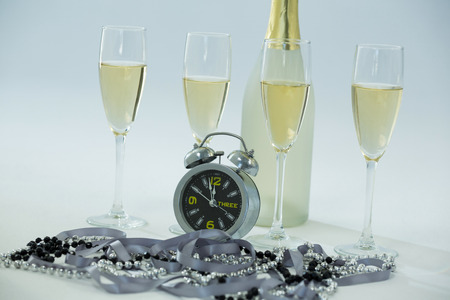 Close-up of champagne with alarm clock and glass on white backgroundの写真素材
