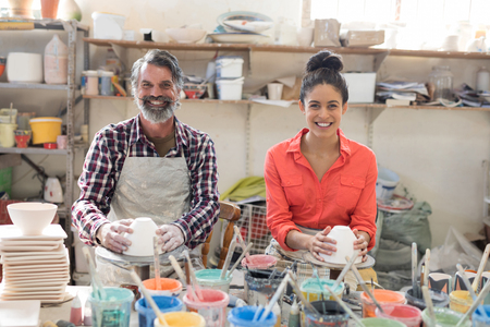 Portrait of male and female potter holding bowl in pottery workshopの写真素材