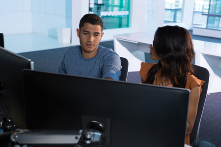 Male and female executive discussing over computer in futuristic office