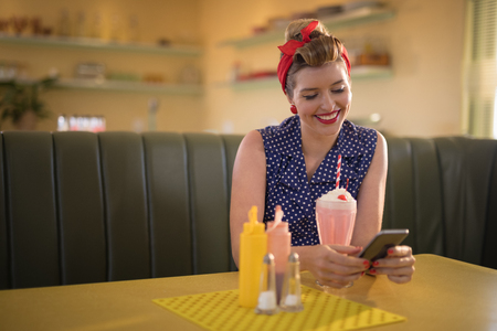 Happy woman using mobile phone in restaurantの写真素材