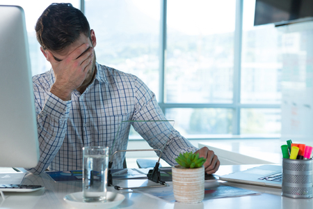 Male executive suffering from headache at desk in officeの写真素材