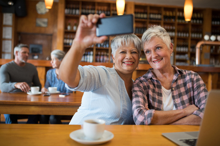 Smiling senior friends taking selfie with mobile phone in restaurantの写真素材