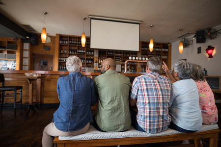 Friends sitting together and watching soccer on projectors in barの写真素材