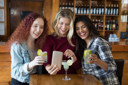 Happy female friends looking their photos on mobile phone in barの写真素材