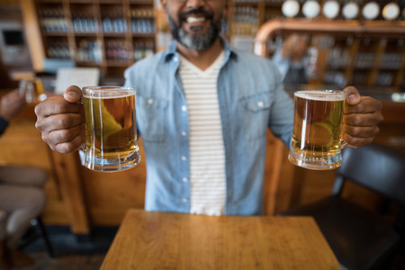 Mid section of smiling man having glasses of beer in restaurant