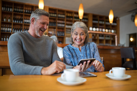 Happy senior couple looking their photos on mobile phone in restaurant