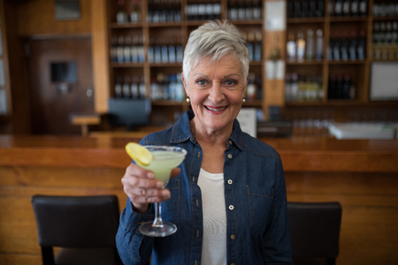 Portrait of smiling senior woman having glass of wine at counter in barの写真素材