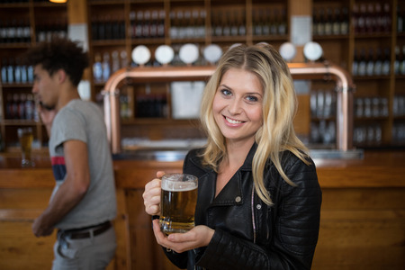 Portrait of smiling beautiful woman holding glass of beer in bar