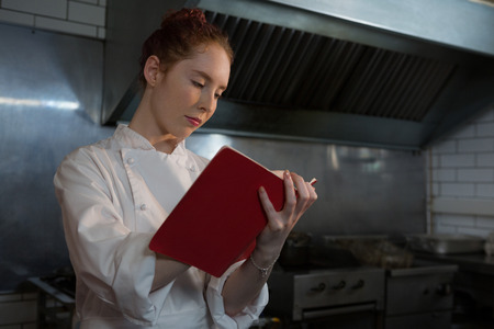 Female chef taking down an order in the book in the kitchenの写真素材
