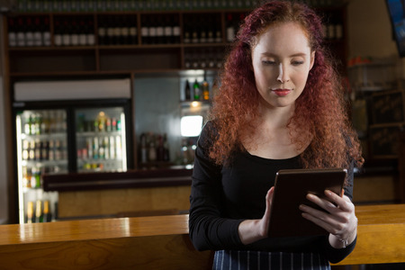 Beautiful waitress using digital tablet near bar counterの写真素材
