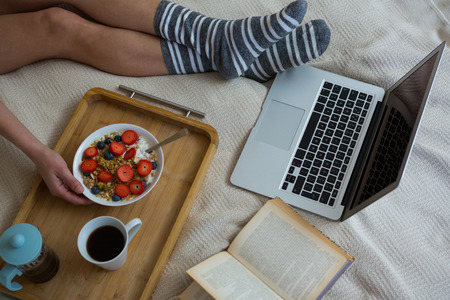 Low section of woman having breakfast on bed in bedroom