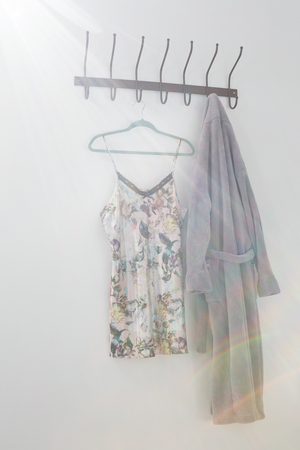 Bathrobe and nightwear hanging on hook against white wallの写真素材
