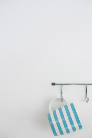 Striped mug hanging on hook against white wallの写真素材
