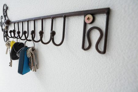 Close-up of various keys hanging on hook against white wallの写真素材