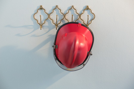 Red hardhat hanging on hook against white wallの写真素材