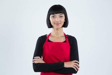 Portrait of smiling waitress standing with arms crossed against white backgroundの写真素材