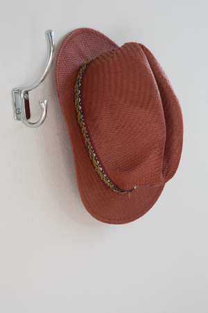 Close-up of hat hanging on hook against white wallの写真素材