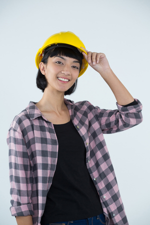 Portrait of female architect in hard hat standing against white backgroundの写真素材