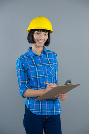 Portrait of smiling female architect writing on clipboard against grey backgroundの写真素材