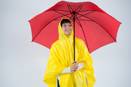 Smiling woman in yellow raincoat holding an umbrellaの写真素材