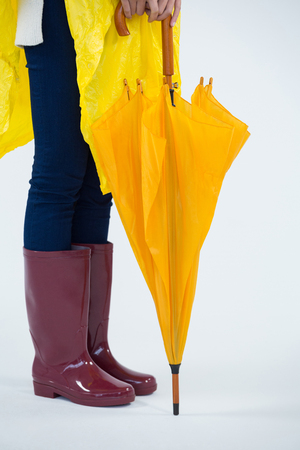 Low section of woman in yellow raincoat holding an umbrellaの写真素材