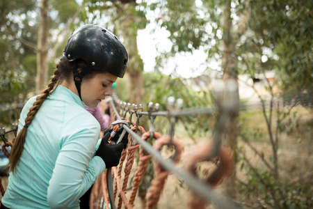 Side view of woman attaching carabiner to rope bridge