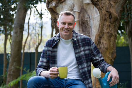 Portrait of smiling man having cup of coffee in gardenの写真素材