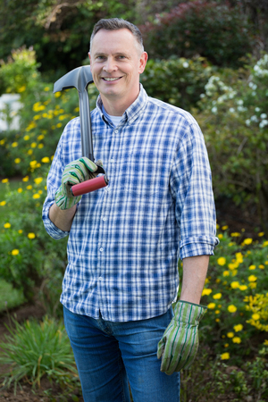 Portrait of smiling man holding gardening tool in gardenの写真素材