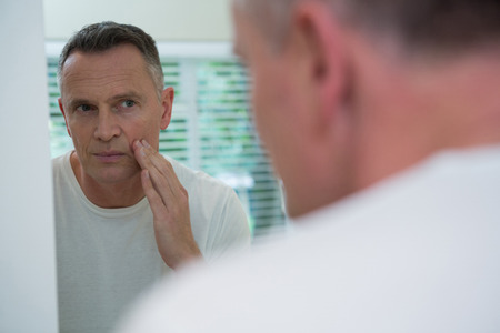 Man looking his face in the mirror after shaving standing in the bathroomの写真素材
