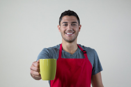 Portrait of smiling waiter offering a cup of coffeeの写真素材