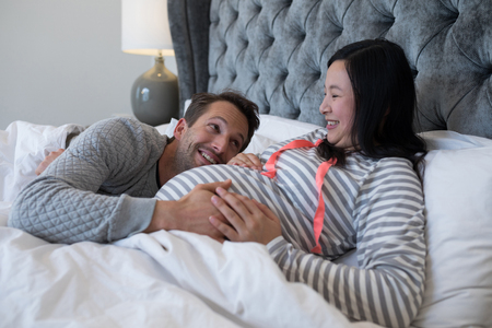 Happy man touching woman stomach in bedroomの写真素材