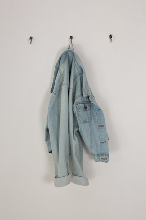 Denim jacket hanging on hook against wallの写真素材