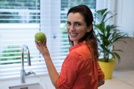 Woman holding a green apple in kitchen at homeの写真素材