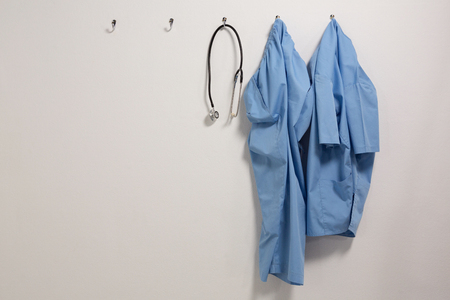 Scrubs and stethoscope hanging on hook against wallの写真素材