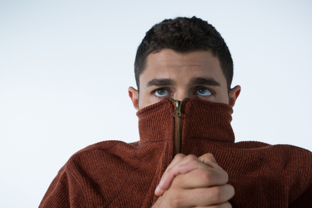 Scared man covering his mouth with turtle neck jacket against white backgroundの写真素材