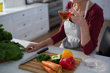 Mid section of woman having lemon tea at table in kitchenの写真素材