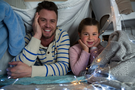 Portrait of happy father and daughter lying in bedroomの写真素材