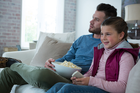 Father and daughter watching television in living room at homeの写真素材