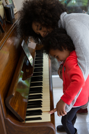 Mother assisting daughter in playing piano at homeの写真素材