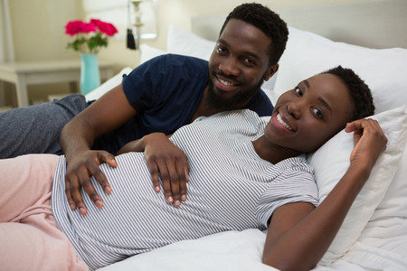 Man touching woman stomach in bedroom at homeの写真素材