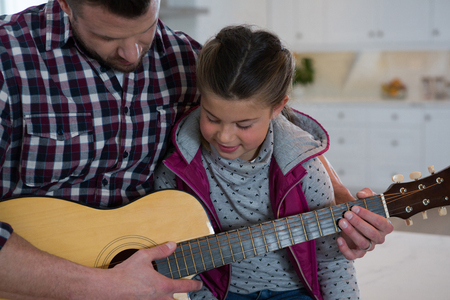 Close-up of father assisting his daughter in playing guitarの写真素材