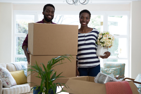 Portrait of couple carrying big cardboard box and vase at new homeの写真素材
