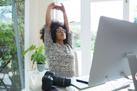 Graphic designer stretching her arms at deskの写真素材
