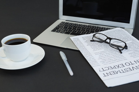Close-up of coffee cup, laptop, spectacles, newspaper and pen on black backgroundの写真素材