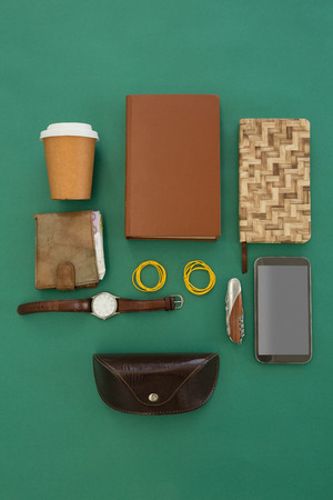 Overhead of disposable glass, organizer, wristwatch, pocketknife, mobile phone and sunglasses case on green backgroundの写真素材
