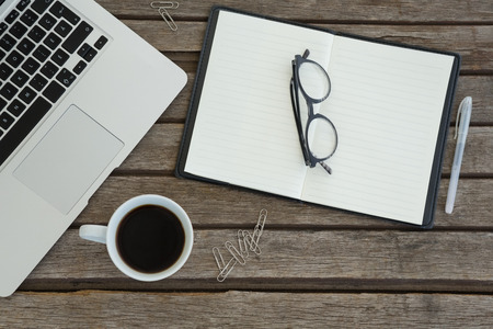 Overhead of organizer, spectacles, pen, black coffee and laptop on wooden plankの写真素材