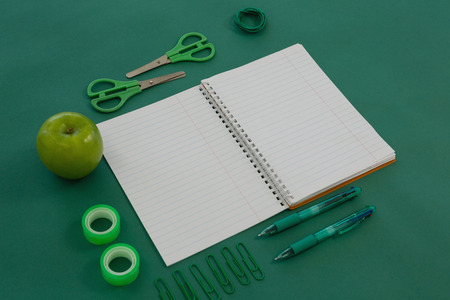 Overhead of office supplies and apple on green background